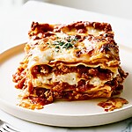A slice of baked lasagna on a white plate showing distinct layers and a golden cheese topping
