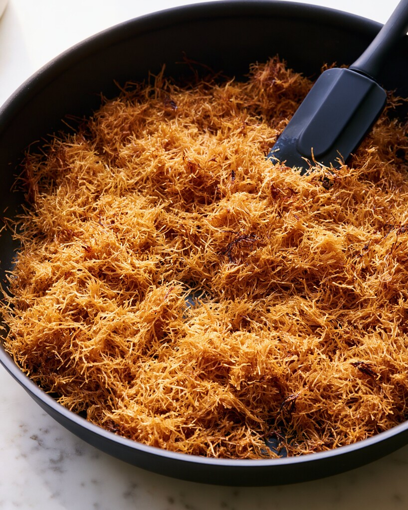 Toasted golden kataifi pastry strands in a black skillet with a silicone spoon