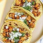 Skillet-crisped chicken street tacos on a light plate topped with diced white onion, cilantro, and crumbled cotija cheese