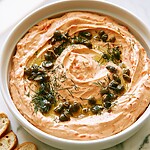 Smooth smoked salmon mousse in a white serving bowl topped with crispy capers, dill sprigs, and a drizzle of oil