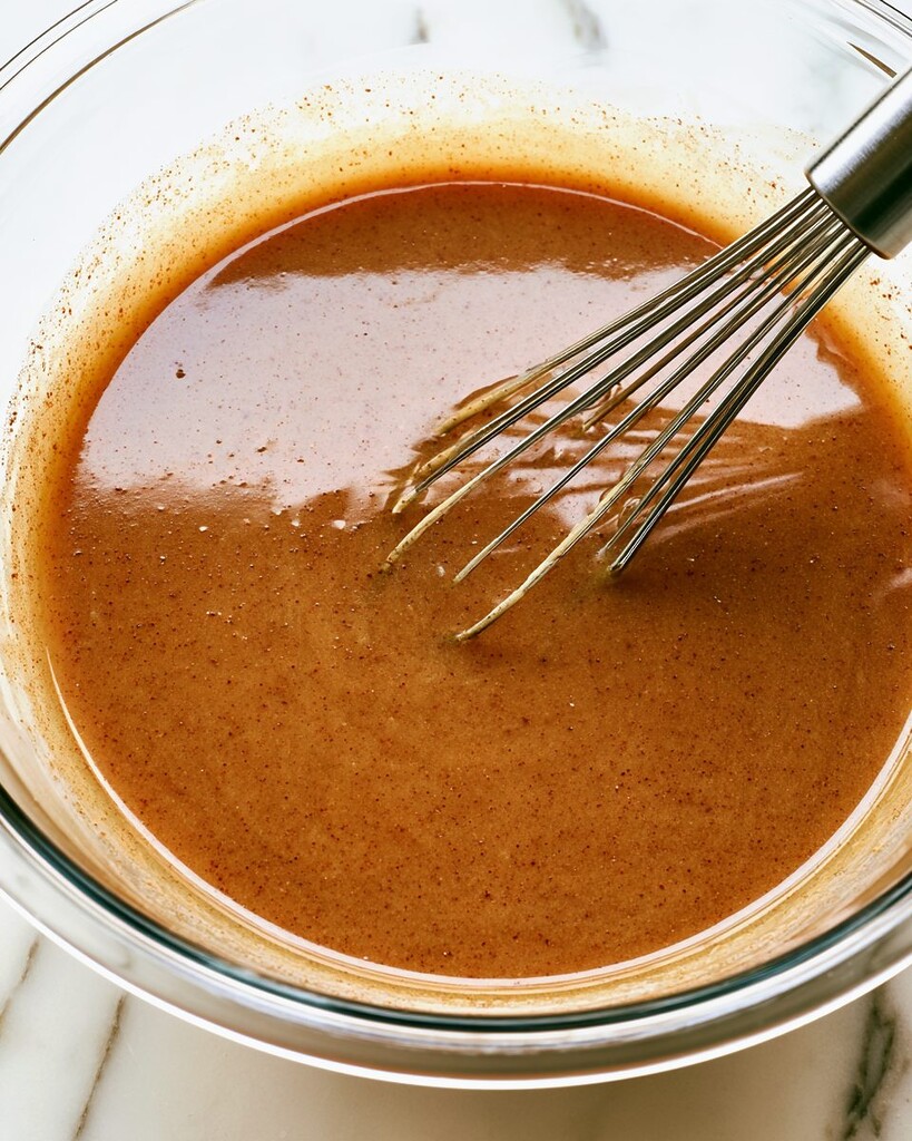 Apple butter pie filling mixed to a smooth brown liquid in a glass bowl with a wire whisk