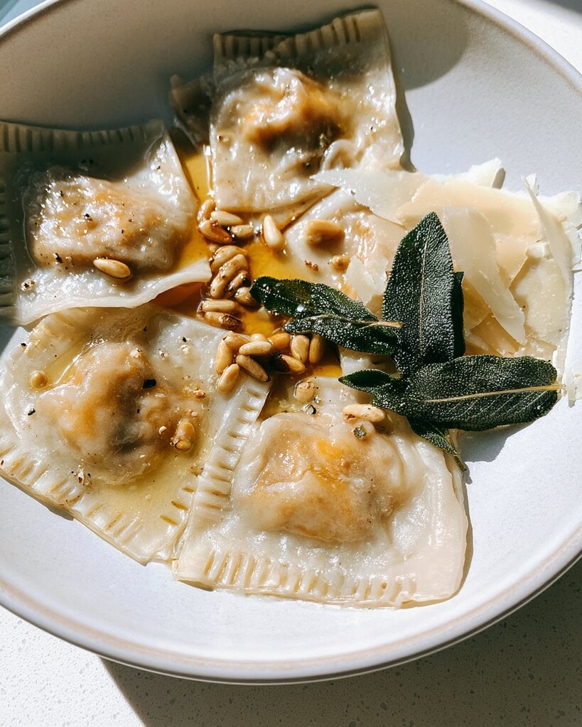 Plated square ravioli garnished with brown butter, pine nuts, parmesan, and fried sage
