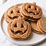 Salted Brown Butter Jack-O'-Lantern Sandwich Cookies Spiced jack-o-lantern sandwich cookies with a golden brown crust on a white plate
