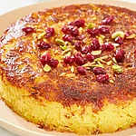 Crispy Persian Baked Rice with Chicken (Tahchin) Golden baked Tahchin on a platter topped with red barberries and pistachios