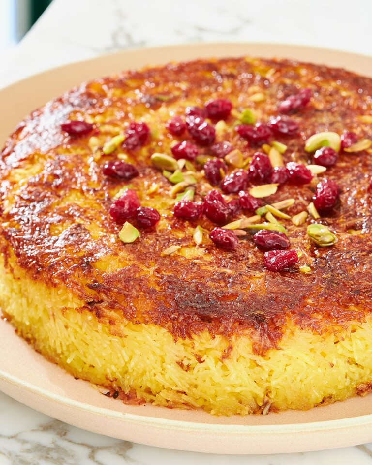 Crispy Persian Baked Rice with Chicken (Tahchin) Golden baked Tahchin on a platter topped with red barberries and pistachios
