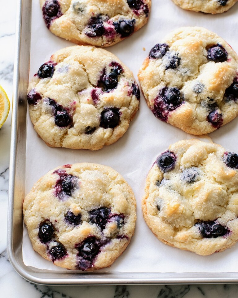 Lemon Blueberry Cookies (No Chill) Thick lemon blueberry cookies with a sparkling sugar crust and visible blueberries resting on a baking sheet