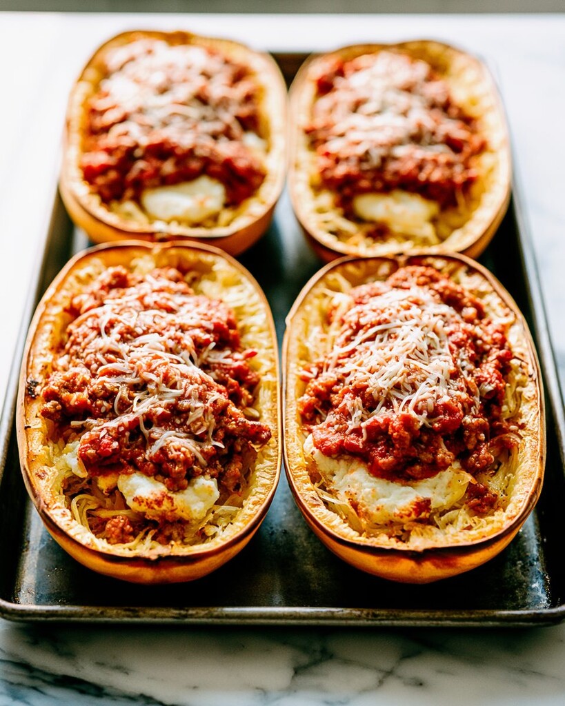 Spaghetti squash halves on a baking tray stuffed with ricotta, meat sauce, and shredded mozzarella cheese