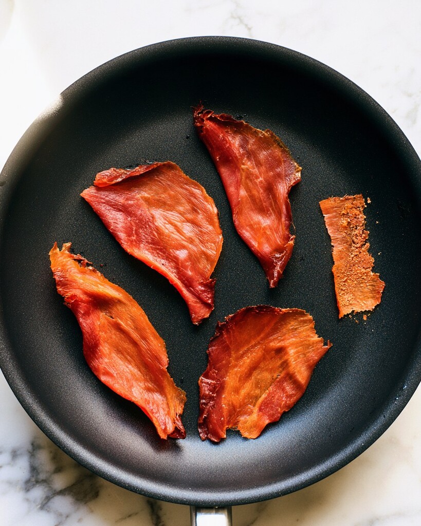Crispy browned prosciutto slices resting in a dark cooking pan