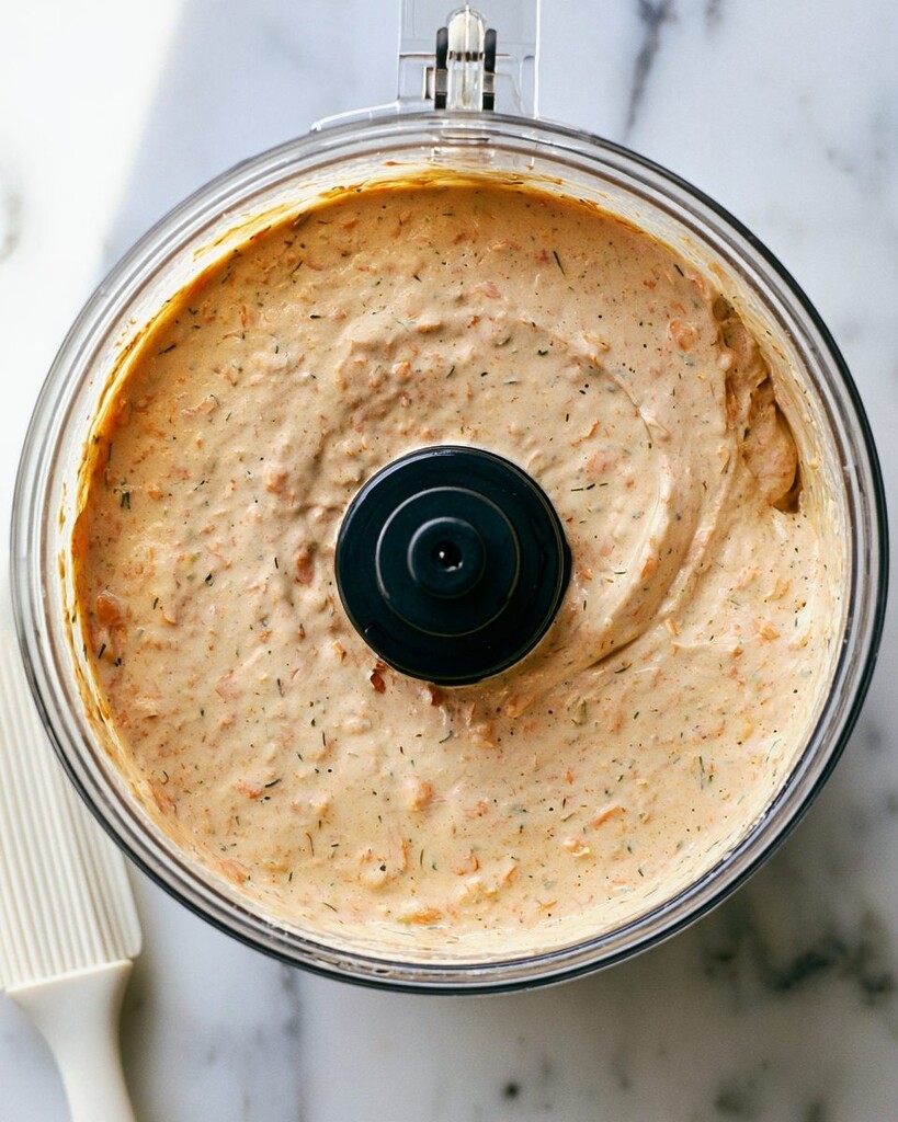 Smoked salmon mixed into the creamy base inside a food processor showing small visible flakes