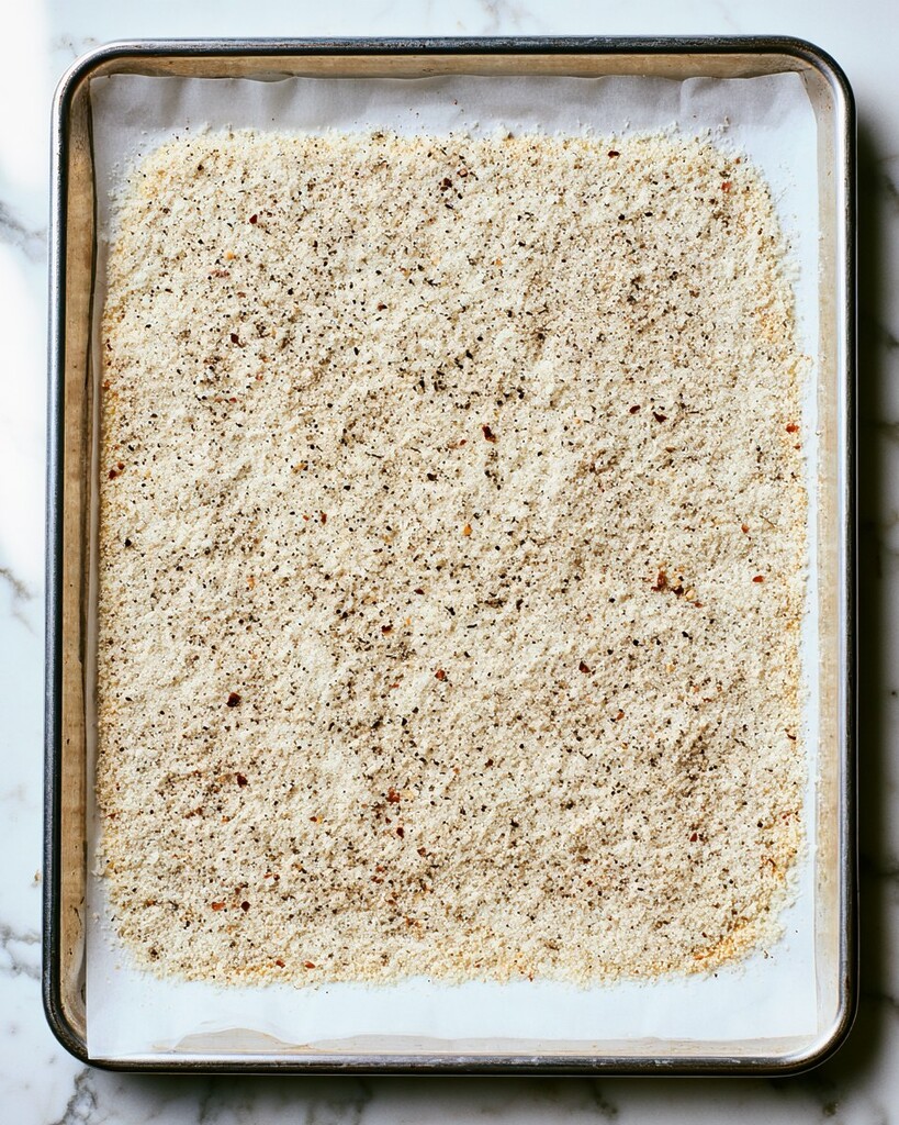 Grated parmesan cheese spread in an even layer on a parchment-lined baking sheet