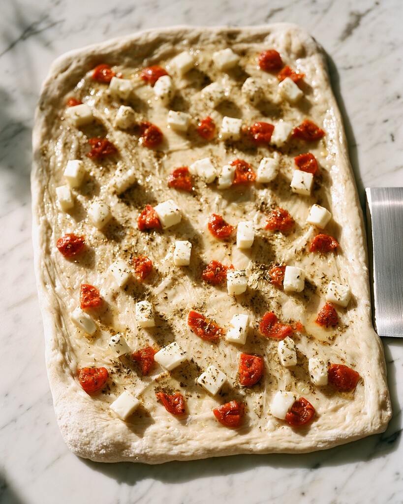 : Sourdough stretched into a rectangle on a marble counter and topped with cubed mozzarella and pepperoni