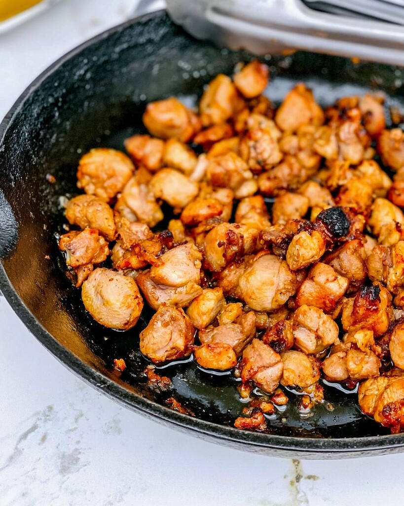Chopped chicken crisping in a black cast-iron skillet with golden-red edges