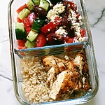 Sliced chicken and rice next to a colorful vegetable salad in a glass container