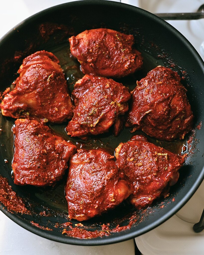 Raw chicken thighs coated in dark red chili-lime marinade in a black skillet