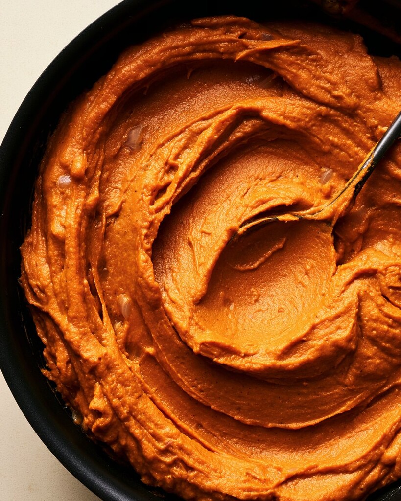 Thick dark orange pumpkin filling spread across a black skillet showing spoon tracks