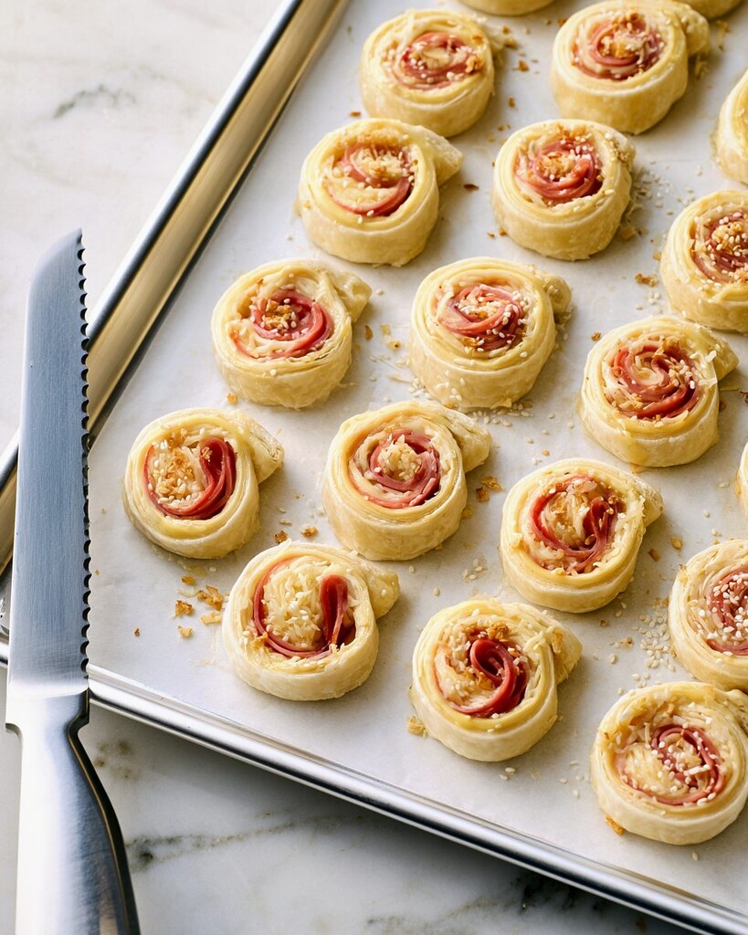 Unbaked ham and cheese pinwheels topped with everything bagel seasoning on a lined baking sheet
