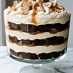 Fully assembled salted caramel brownie trifle topped with cream and pretzels in a glass bowl