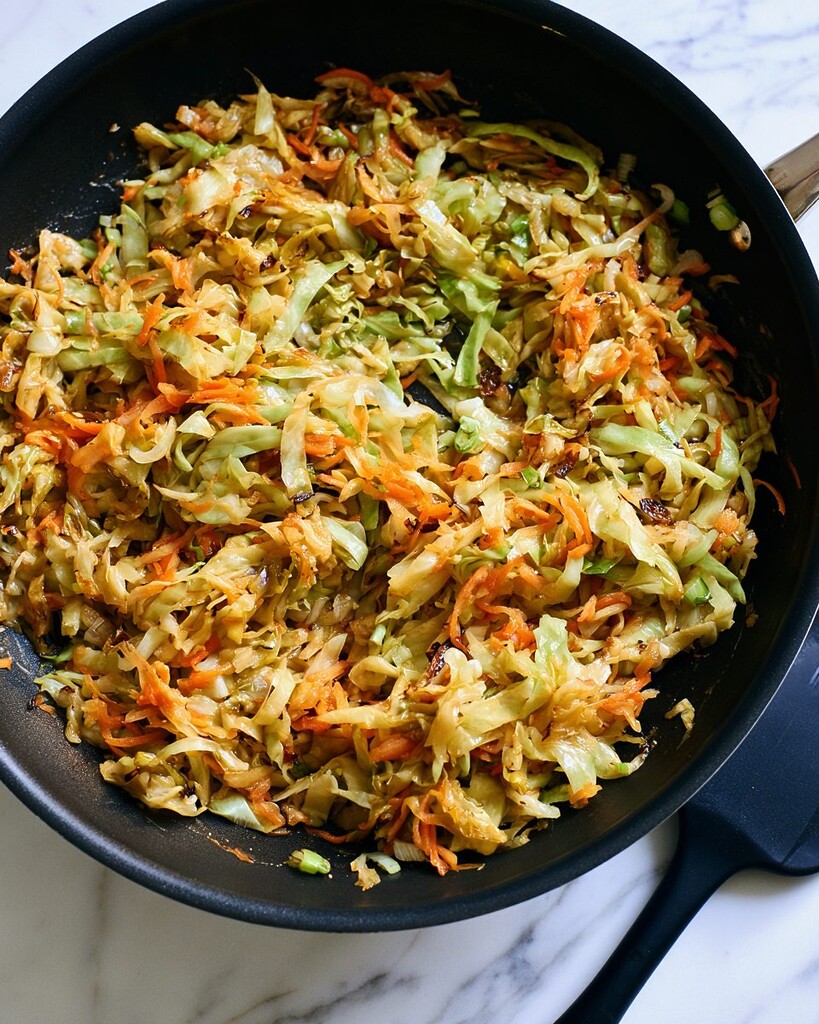 Shredded cabbage and grated carrots cooking down in a black skillet