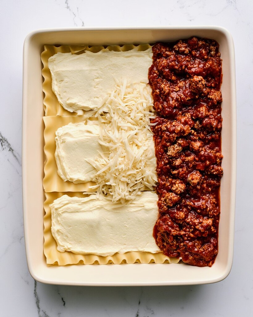 Layering lasagna noodles, meat sauce, and cheese in a rectangular ceramic baking dish