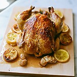 Garlic Herb Roast Chicken: The Two-Temperature Method Garlic herb roast chicken on a wooden cutting board surrounded by blistered lemon slices and roasted garlic