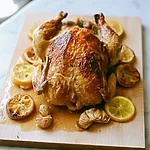 Garlic Herb Roast Chicken: The Two-Temperature Method Garlic herb roast chicken on a wooden cutting board surrounded by blistered lemon slices and roasted garlic