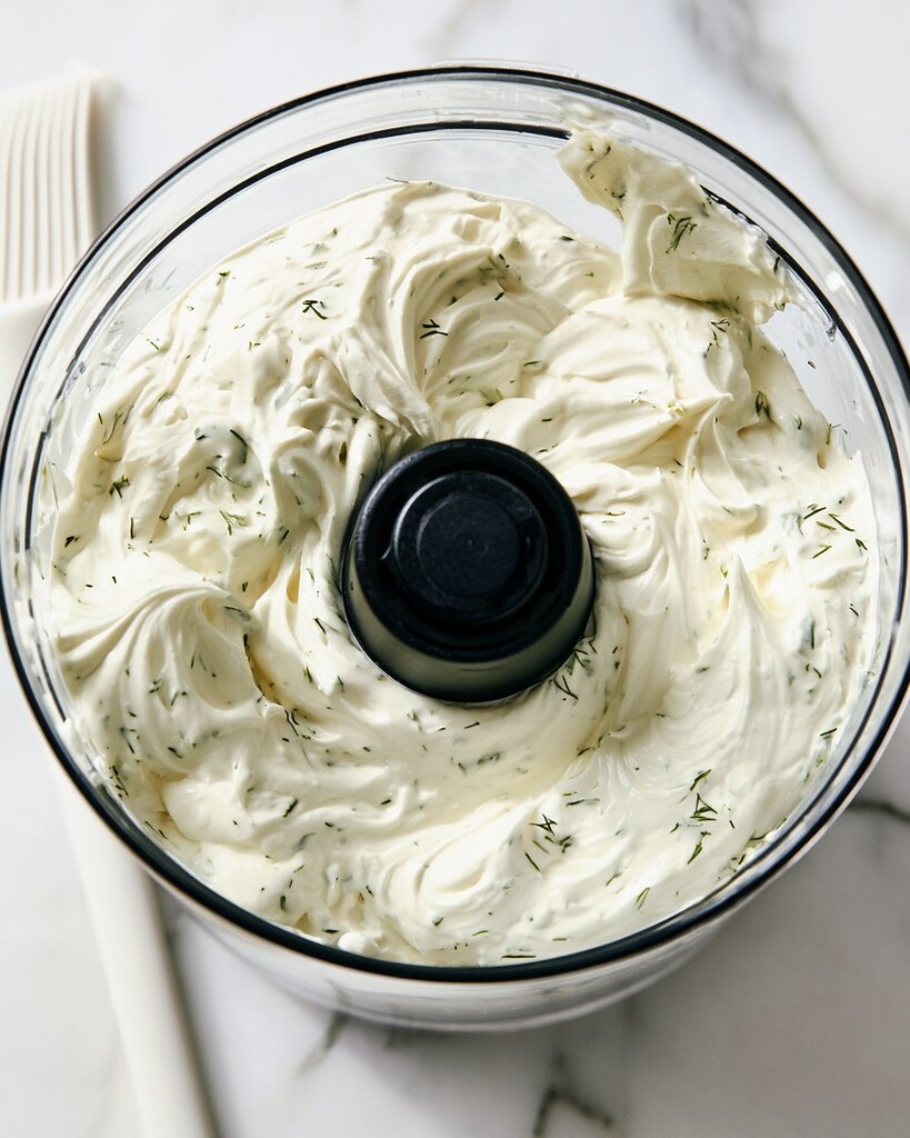 Whipped cream cheese base in a food processor looking white and airy with green dill specks
