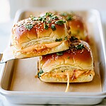 Hot Honey Chipotle Chicken Sliders on Hawaiian Rolls Hot honey chipotle chicken sliders with glossy glazed tops, melted cheese, and toasted sesame seeds on a platter.