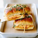 Hot Honey Chipotle Chicken Sliders on Hawaiian Rolls Hot honey chipotle chicken sliders with glossy glazed tops, melted cheese, and toasted sesame seeds on a platter.