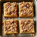 Brown Butter Lemon Crumb Bars Four brown butter lemon crumb bars arranged on a small tray, topped with crisp oat topping and fresh zest