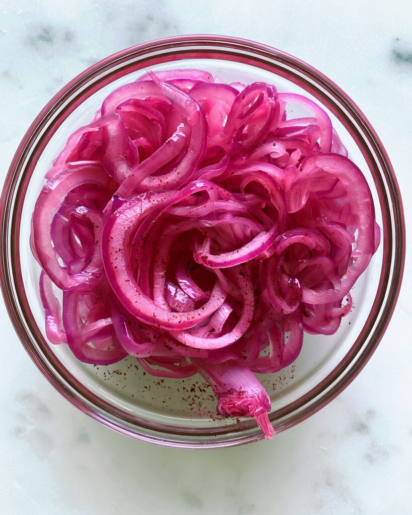 Thinly sliced red onions tossed with sumac and lemon juice in a clear glass bowl