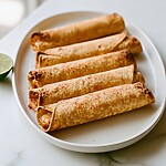 One baked beef taquito served on a white plate beside a fresh half lemon