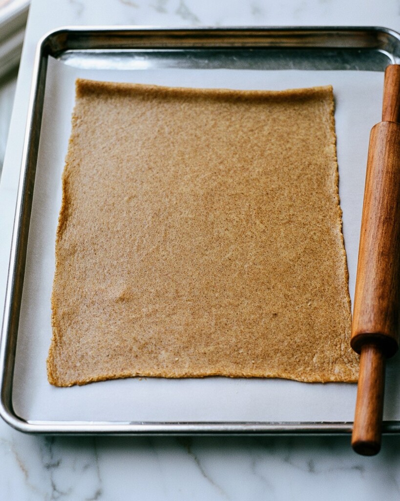 Spiced cookie dough rolled out evenly between parchment paper with a wooden rolling pin