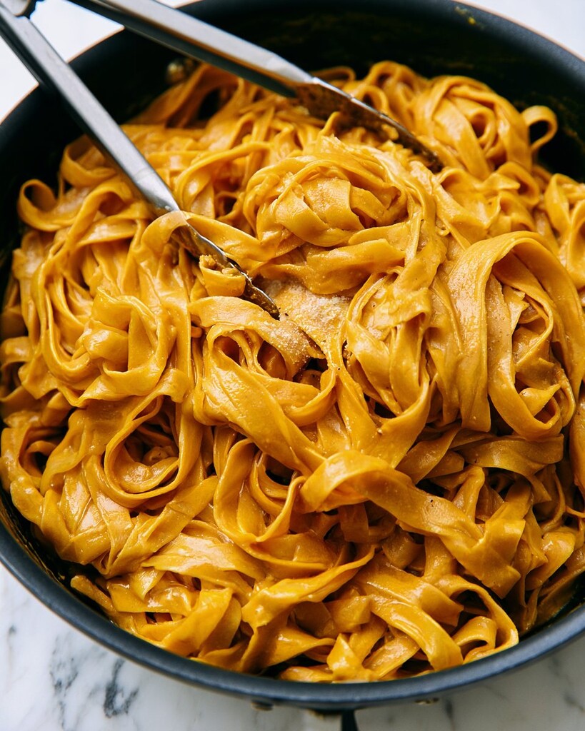 Tossing fettuccine ribbons in the bright orange alfredo sauce using tongs