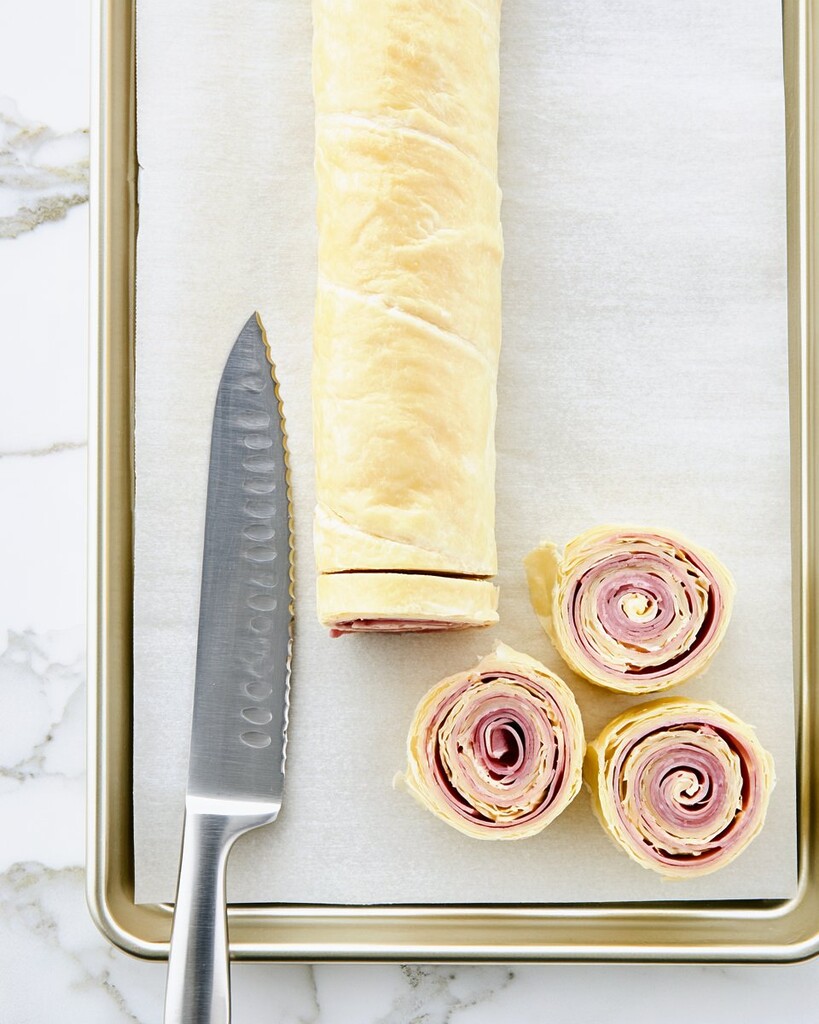 Rolled ham and cheese puff pastry log alongside sliced spirals and a serrated knife