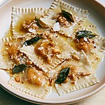 Ceramic plate filled with pumpkin wonton ravioli, parmesan flakes, pine nuts, and sage