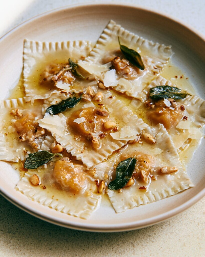 Ceramic plate filled with pumpkin wonton ravioli, parmesan flakes, pine nuts, and sage