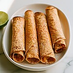 Baked Beef Taquitos with Chili-Lime Crust Four baked beef taquitos arranged neatly on a white plate, showcasing a deeply toasted, chili-lime dusted crust.