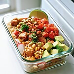 Finished chili-lime chicken meal prep bowl topped with pico de gallo and an avocado half sprinkled with Tajín