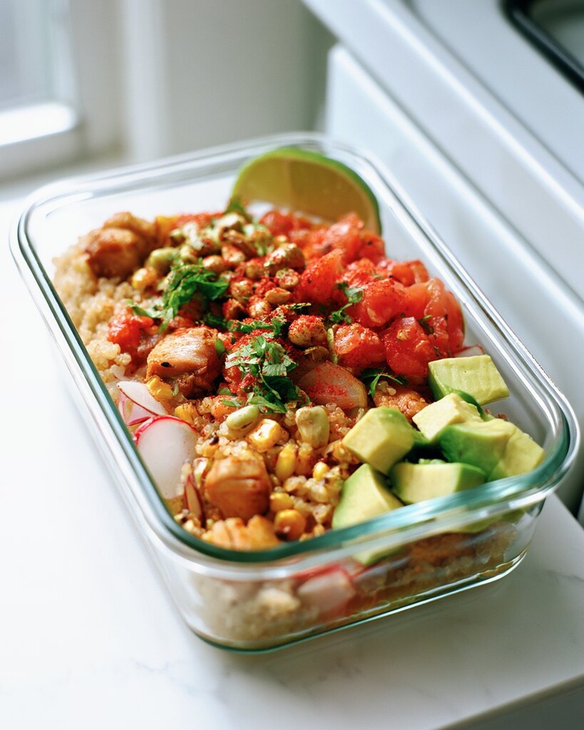 Finished chili-lime chicken meal prep bowl topped with pico de gallo and an avocado half sprinkled with Tajín