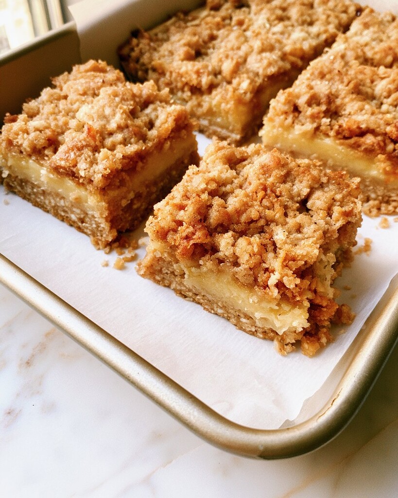 Close up of a lemon bar square showing a thick yellow filling and a toasted oat crumb layer