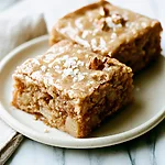 Chewy Salted Maple Brown Butter Apple Blondies Two salted maple brown butter apple blondies on a light plate showing a shiny glazed surface and dense centers