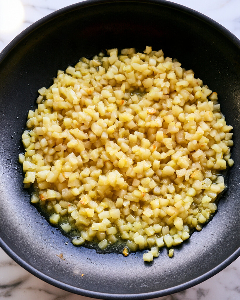 Diced apples cooking in a black skillet until soft