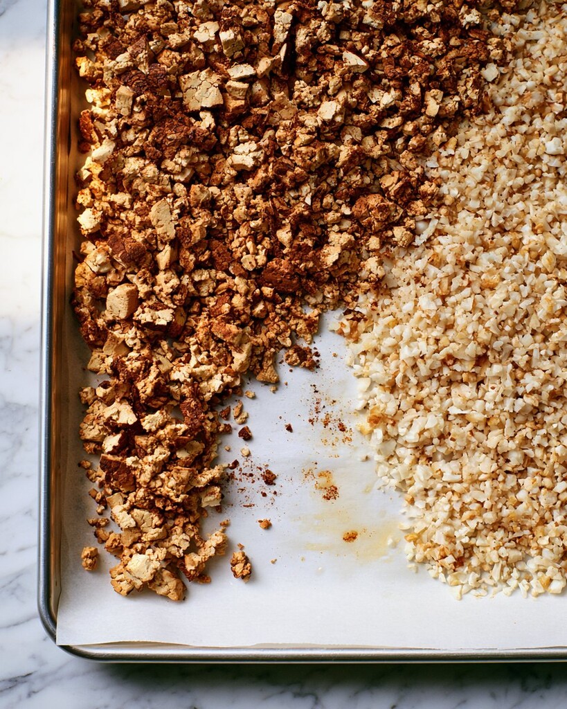 Spiced tofu crumbles and frozen cauliflower rice spread evenly on opposite sides of a parchment-lined baking sheet