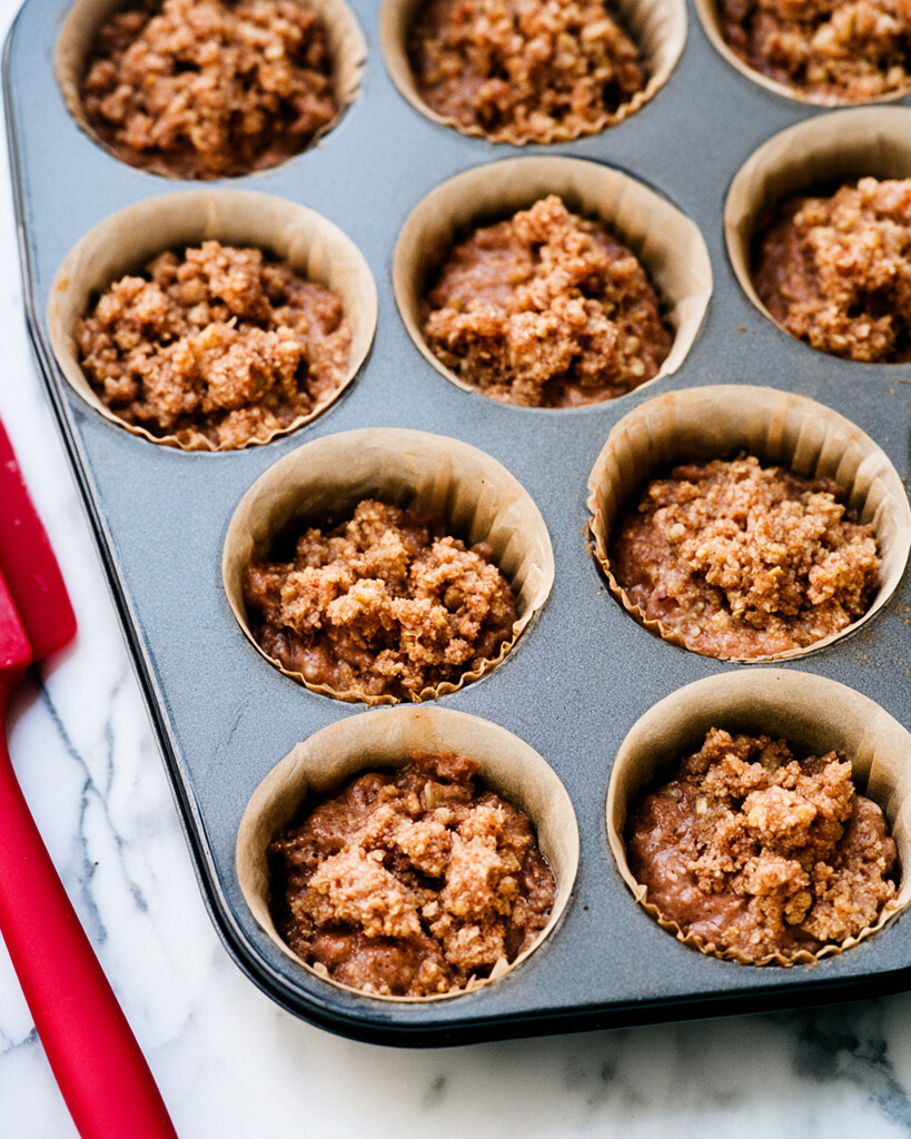 Apple cider doughnut muffin batter in paper liners finished with a coarse brown streusel topping