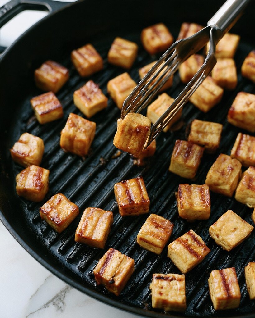 Teriyaki tofu cubes cooking in a hot grill pan with distinct grill marks