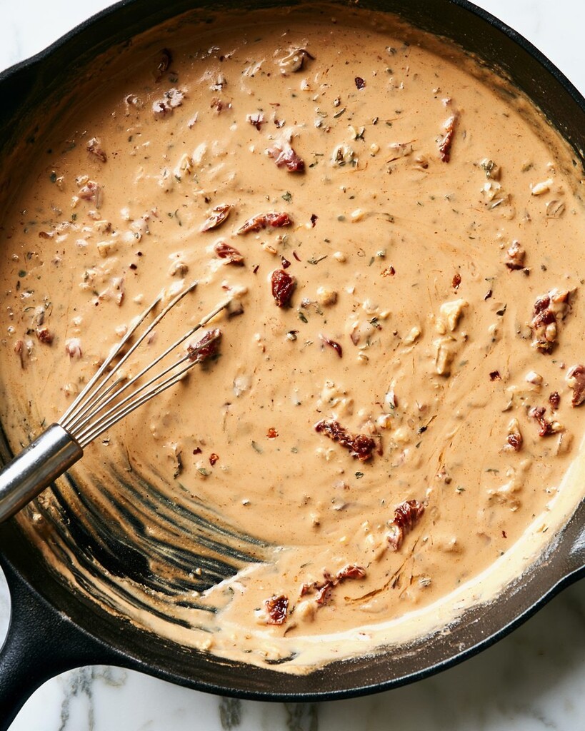 Creamy sun-dried tomato sauce being whisked in a cast-iron skillet