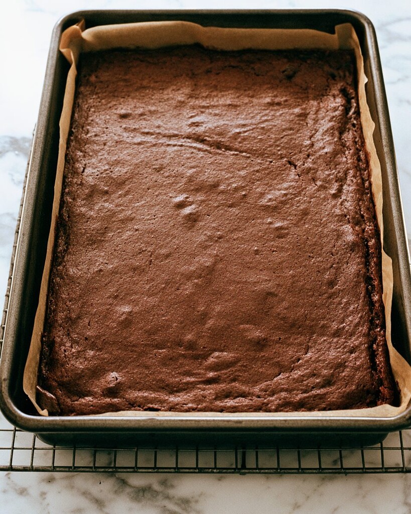 Baked dark chocolate cake sitting in a parchment-lined rectangular baking pan