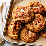 Chewy Brown Butter Pumpkin Snickerdoodles Stacked brown butter pumpkin snickerdoodles on a tray, with one broken piece showing a chewy center