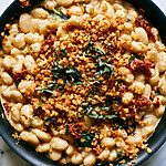 Black skillet filled with creamy white beans topped with golden panko crumbs and fresh basil