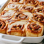 Golden rolls in a white dish covered with thick cream cheese icing and caramel ribbons